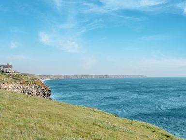A coastal cliff with a house on the edge overlooking the sea and a grassy field at Loe Cottage in Porthleven