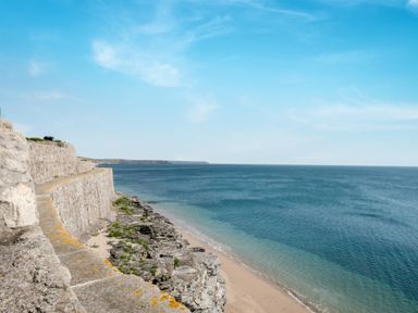 A coastal view of a stone seawall along a rocky beach with the ocean and blue sky at Loe Cottage in Porthleven