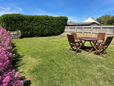A garden with wooden table and chairs on grass surrounded by flowers and a wooden fence at The Old Boathouse in Trefin near St Davids