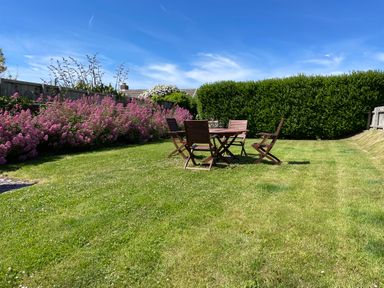 A grassy garden with a wooden table and four chairs surrounded by flowering plants and hedges at The Old Boathouse in Trefin near St Davids