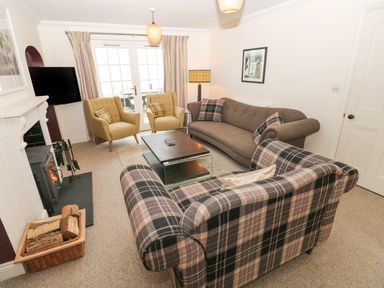 A living room with sofas, armchairs, a coffee table, a fireplace, and a television at The Old Boathouse in Trefin near St Davids