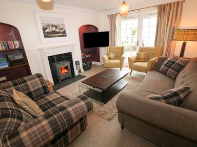 A living room with plaid sofas yellow armchairs a fireplace and a coffee table at The Old Boathouse in Trefin near St Davids