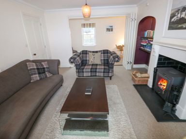 A living room with two sofas a coffee table a wood burning stove and a bookshelf at The Old Boathouse in Trefin near St Davids