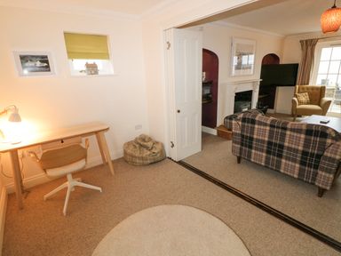 A room with a desk, chair, and bean bag next to a living area with a plaid sofa, armchair, fireplace, and television at The Old Boathouse in Trefin near St Davids