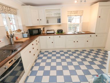 A kitchen with white cabinets wooden countertops checkered blue and white floor and appliances at The Old Boathouse in Trefin near St Davids