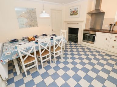 A kitchen with a dining table set for six people blue and white checkered floor at The Old Boathouse in Trefin near St Davids