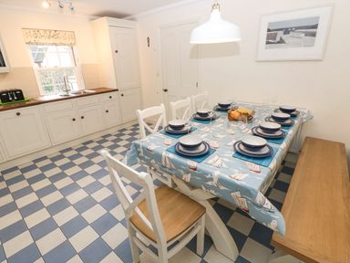 A kitchen with a dining table set for eight people and checkered floor at The Old Boathouse in Trefin near St Davids