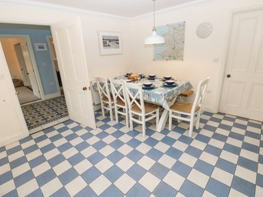 A dining room with a table set for six with white chairs and checkered blue and white floor tiles at The Old Boathouse in Trefin near St Davids