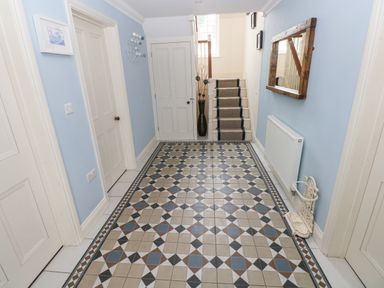A hallway with patterned tiled floor blue walls doors a mirror radiator and stairs at The Old Boathouse in Trefin near St Davids