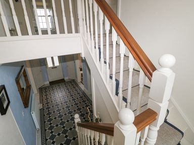 A staircase with white banisters and wooden handrails above a hallway with patterned tile flooring and a white front door at The Old Boathouse in Trefin near St Davids