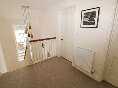 A stair landing with carpet flooring a white banister pendant lights a radiator and framed art at The Old Boathouse in Trefin near St Davids