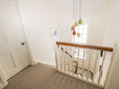 A carpeted stair landing with white wooden banisters and a window with colorful hanging lights at The Old Boathouse in Trefin near St Davids