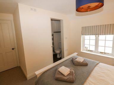 A bedroom with a bed and towels on it a door opening to a bathroom and a window with a striped blind at The Old Boathouse in Trefin near St Davids