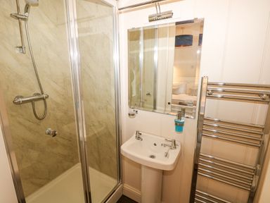 A bathroom with a glass shower cubicle a white sink with a mirror above and a chrome towel radiator at The Old Boathouse in Trefin near St Davids
