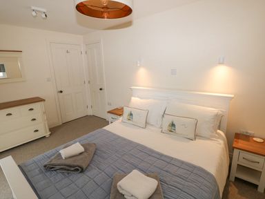 A bedroom with a bed with pillows and folded towels bedside tables a dresser and two doors at The Old Boathouse in Trefin near St Davids