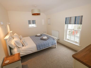 A bedroom with a double bed dresser nightstand and two windows with striped blinds at The Old Boathouse in Trefin near St Davids