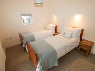 A bedroom with two single beds each with a pillow and light blue blanket and two wooden nightstands at The Old Boathouse in Trefin near St Davids
