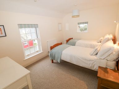 A bedroom with two single beds a window a wooden nightstand and a white table at The Old Boathouse in Trefin near St Davids