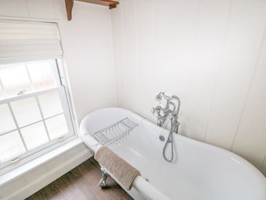 A white bathroom with a clawfoot bathtub and a window with a white blind at The Old Boathouse in Trefin near St Davids