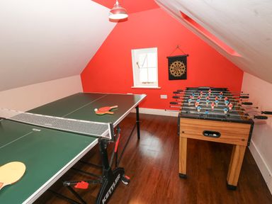 A game room with a table tennis table and a foosball table with a dartboard on the wall at The Old Boathouse in Trefin near St Davids