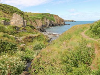 A coastal landscape with green hills rocky cliffs a small stream and a stone ruin near the sea at The Old Boathouse in Trefin near St Davids