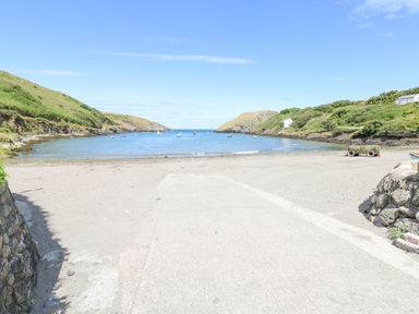 A beach with a concrete ramp leading to the water and boats anchored in a small bay at The Old Boathouse in Trefin near St Davids