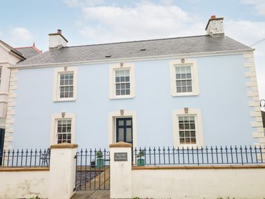 A blue two-story house with white trim and a black front door behind a blue metal fence at The Old Boathouse in Trefin near St Davids