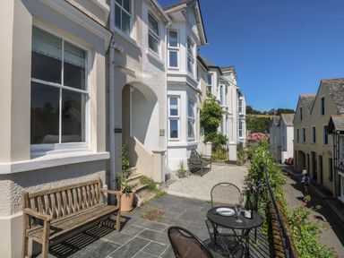 A front patio area with wooden bench metal table and chairs outside white buildings on a street at 21 Passage Street formerly Panacea in Fowey