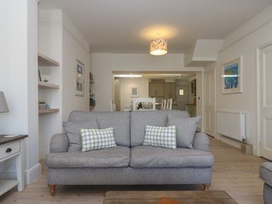 A living room with a grey sofa and polka dot cushions with a view into a dining area and kitchen at 21 Passage Street formerly Panacea in Fowey