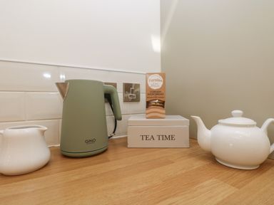 A kitchen counter with a green electric kettle creamer jug white teapot and a box labeled tea time with biscuits on top at 21 Passage Street formerly Panacea in Fowey