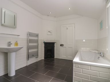 A bathroom with a sink mirror radiator bathtub and door at 21 Passage Street formerly Panacea in Fowey