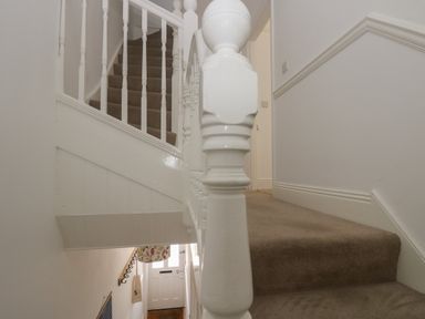 A carpeted staircase with white wooden banisters and a white door at the bottom at 21 Passage Street formerly Panacea in Fowey