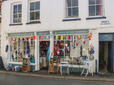 A shopfront with chairs tables hats and colorful flags hanging above at 21 Passage Street formerly Panacea in Fowey
