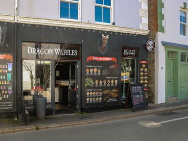 A storefront with dragon decor and signs for Dragon Waffles and boozy milkshakes at 21 Passage Street formerly Panacea in Fowey
