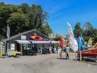A kayak rental shop with kayaks outside and people walking near the entrance at 21 Passage Street formerly Panacea in Fowey