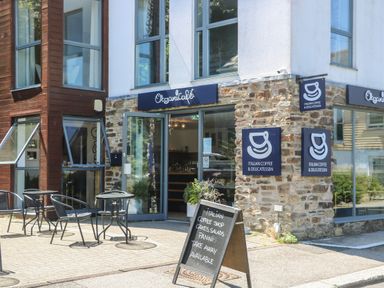 An outdoor seating area with metal tables and chairs in front of a stone and glass coffee shop at 21 Passage Street formerly Panacea in Fowey
