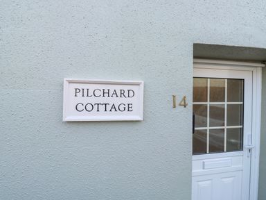 A white door with glass window and house number 14 next to a sign saying Pilchard Cottage in Dawlish
