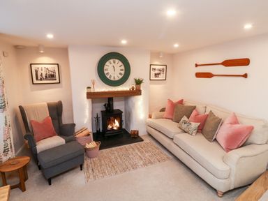A living room with a sofa, armchair, fireplace, clock, and wooden paddles on the wall at Pilchard Cottage in Dawlish