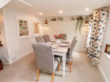 A dining room with a table set for six with floral centerpiece and patterned curtains at Pilchard Cottage in Dawlish