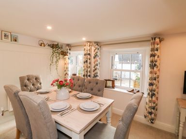 A dining room with a wooden table set for six people and floral curtains at Pilchard Cottage in Dawlish