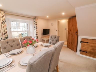 A dining area with a table set for four and a vase of flowers near a window at Pilchard Cottage in Dawlish