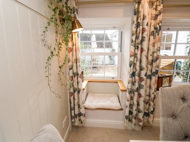 A window seat with a cushion and floral curtains in a living room at Pilchard Cottage in Dawlish