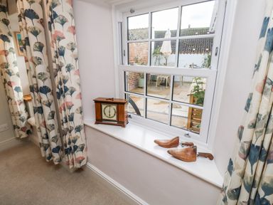 A window with a wooden clock and shoe stretchers on the sill with floral curtains at Pilchard Cottage in Dawlish