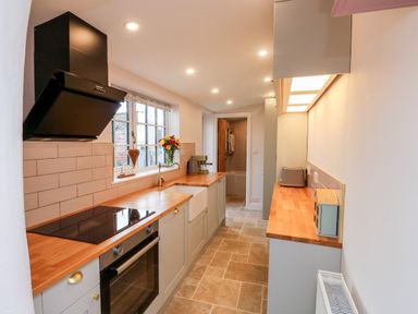 A kitchen with wooden countertops oven sink and window with flowers at Pilchard Cottage in Dawlish