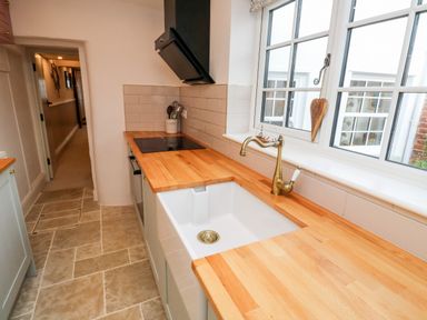 A kitchen with wooden countertops a white sink a brass faucet and a window at Pilchard Cottage in Dawlish