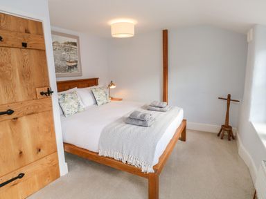 A bedroom with a wooden bed frame two pillows two folded towels a bedside lamp and a wooden door at Pilchard Cottage in Dawlish
