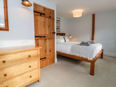 A bedroom with a wooden bed and dresser a wooden door and gray carpet at Pilchard Cottage in Dawlish