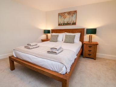A bedroom with a wooden bed frame two bedside tables with lamps and a painting above the bed at Pilchard Cottage in Dawlish