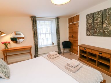 A bedroom with a bed folded towels wooden desk with flowers round mirror wooden cabinet and a chair at Pilchard Cottage in Dawlish