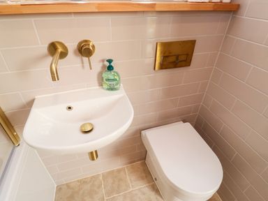 A small bathroom with a white sink and toilet with gold fixtures and beige tiled walls at Pilchard Cottage in Dawlish
